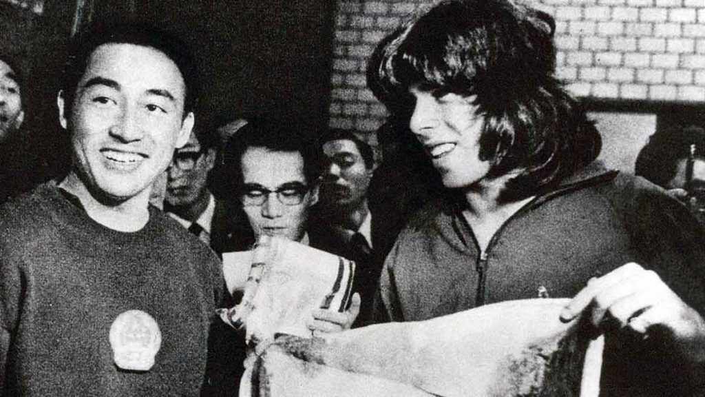 Der dreimalige chinesische Tischtennis-Weltmeister Zhuang Zedong (links) überreicht dem amerikanischen Athleten Glenn Cowan (rechts)